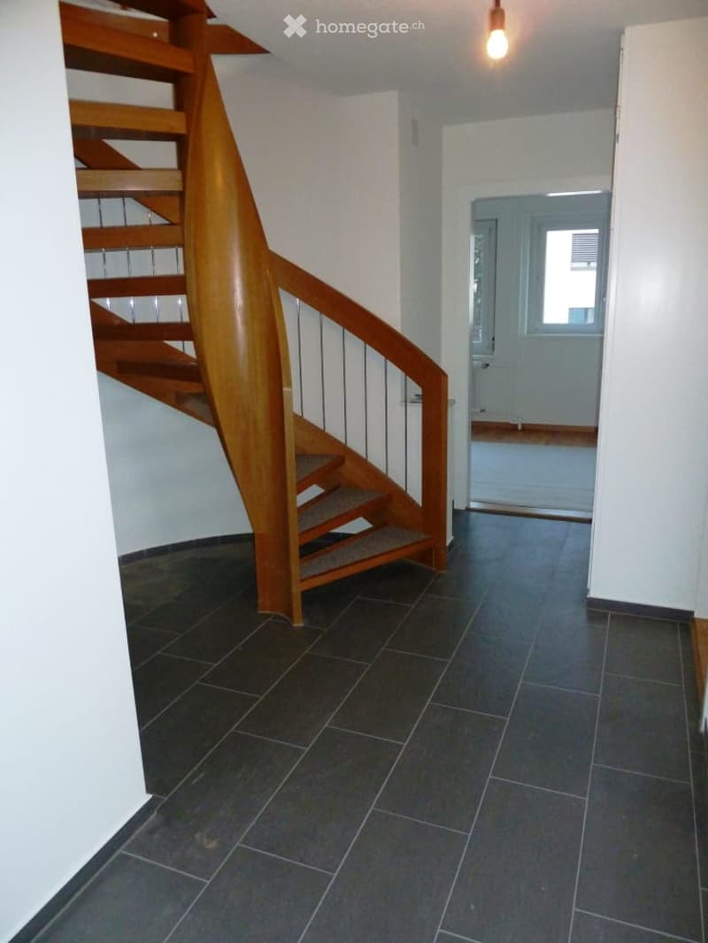 Entrance hall with wooden spiral staircase, tiled floor, white walls, open door to another room
