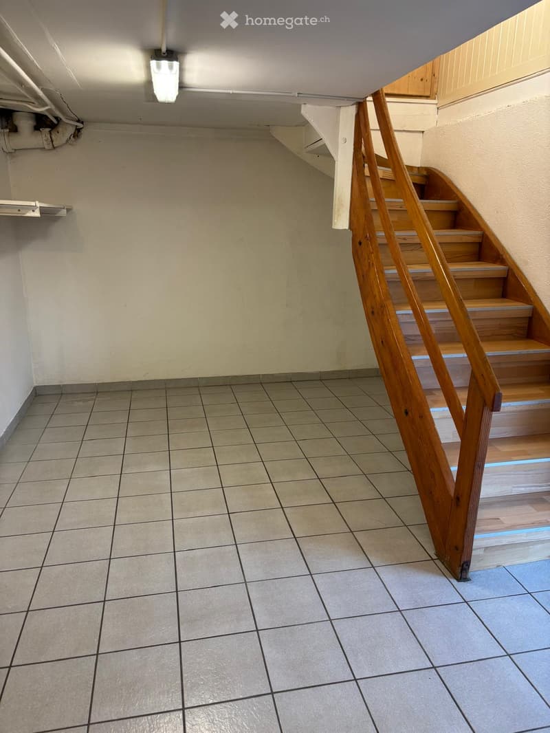 Empty room with tiled floor, wooden staircase, white walls, ceiling light