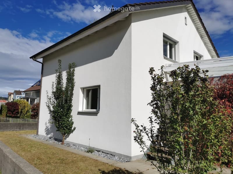 White house, brown roof, three windows, small garden, gravel path