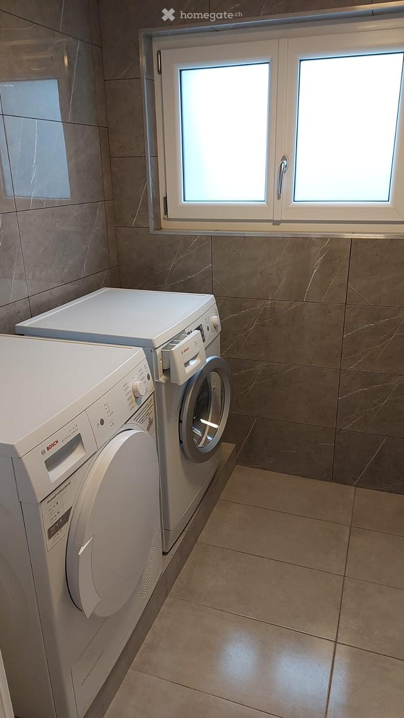 Two white washing machines, tiled floor, window with white frame