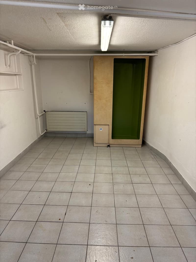 Empty room with white tiled floor, white walls, a white radiator, a wooden storage unit, and a green shower enclosure.
