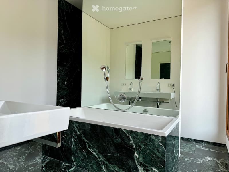 modern bathroom with green marble tiles, bathtub, double sink, mirrors, shower head