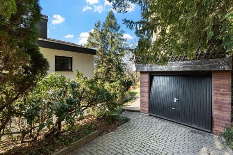 2-story house with a garage, surrounded by trees and greenery