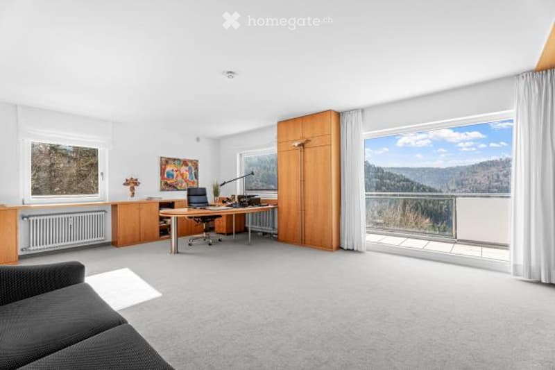Spacious home office with large windows overlooking a scenic landscape, wooden desk and cabinets, comfortable sofa, and artwork on the walls.