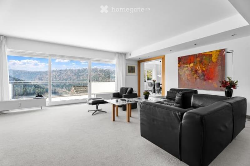 Spacious living room with large windows offering a scenic view, black leather sofas, coffee table, and a colorful abstract artwork on the wall.