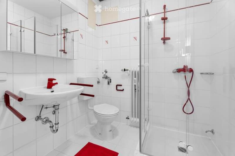 White tiled bathroom with red accents, including a sink, toilet, and shower enclosure.