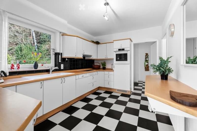 Spacious kitchen with white cabinets, wooden countertops, black and white checkered tile floor, and a dishwasher visible.