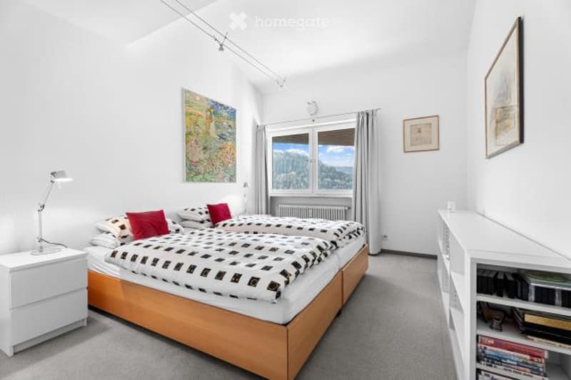 Spacious bedroom with large windows offering a scenic view, white walls, wooden bed frame, bedside tables, and shelving unit for storage.
