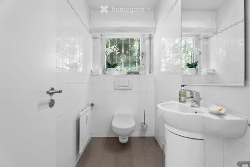 White tiled bathroom with large window, toilet, sink, and mirror