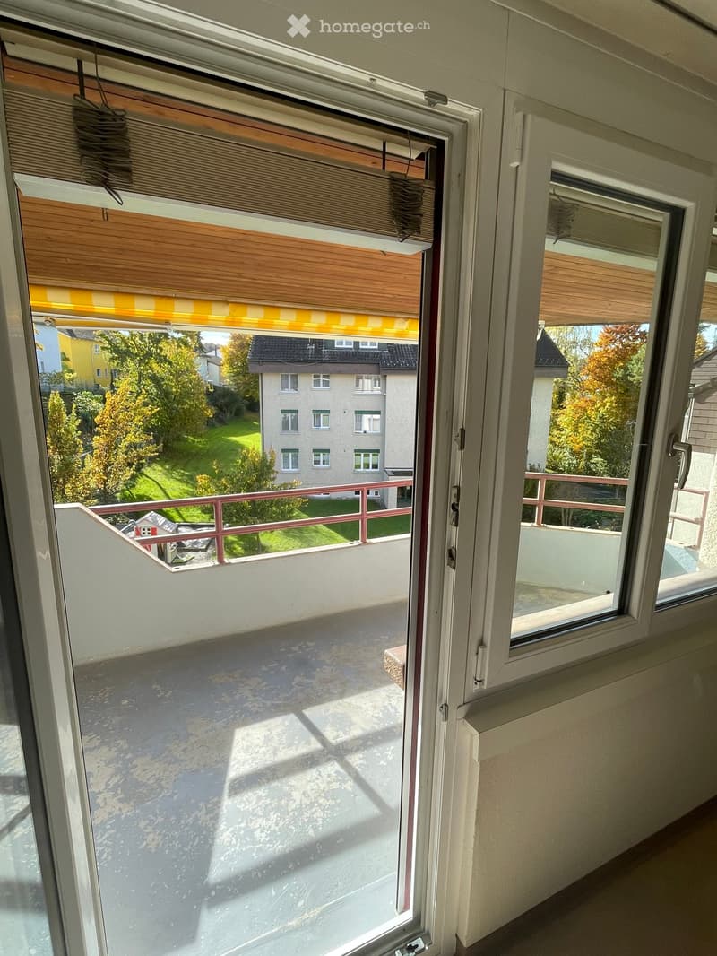 French doors open to terrace, sliding windows, balcony with red railing, yellow striped awning, view of garden and building