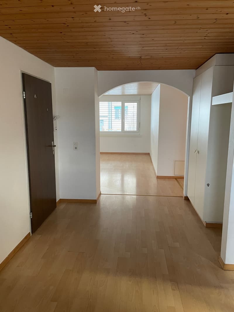 empty room with hardwood floors, white walls, an arched doorway, and a large window with shutters