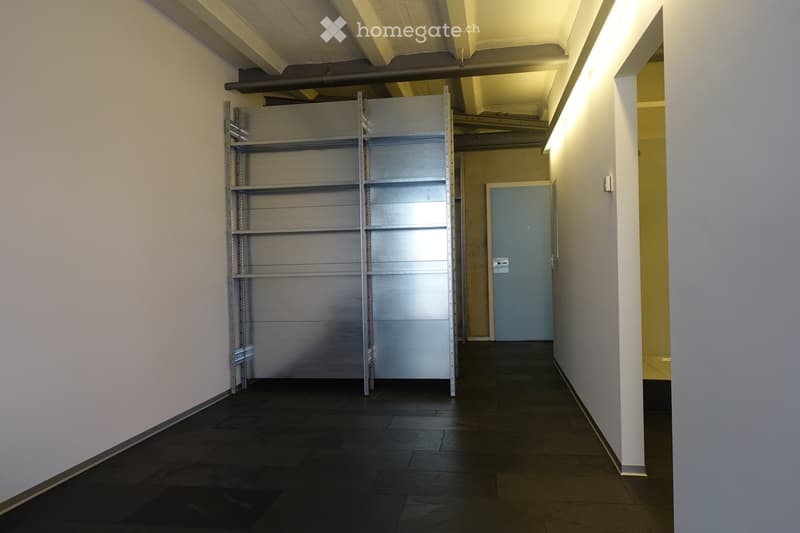 Empty room with white walls, black tiled floor, metal shelving unit, and a door.