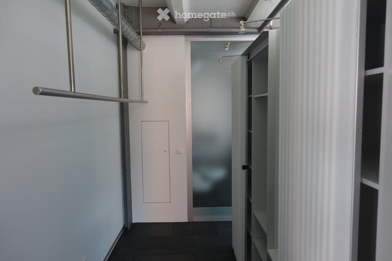 Empty hallway with white walls, black floor, white door, metal pipe, shelves, and lights