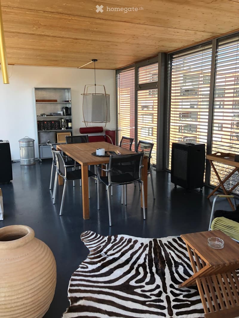 Dining room with wooden table, chairs, zebra rug, large windows, wooden ceiling, trash can, shelf, lamp