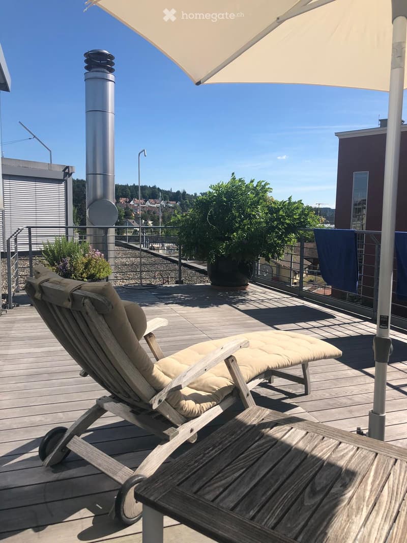 wooden deck, lounge chair, table, umbrella, potted plants, railing, distant view of buildings and trees