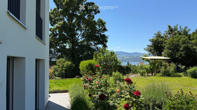 Well-maintained garden with a variety of flowers, shrubs, and trees, featuring a clear view of a lake and distant mountains.