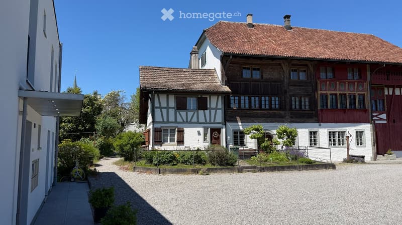 Traditional Swiss-style houses with red-tiled roofs, white walls, and wooden balconies, surrounded by a gravel driveway and greenery.