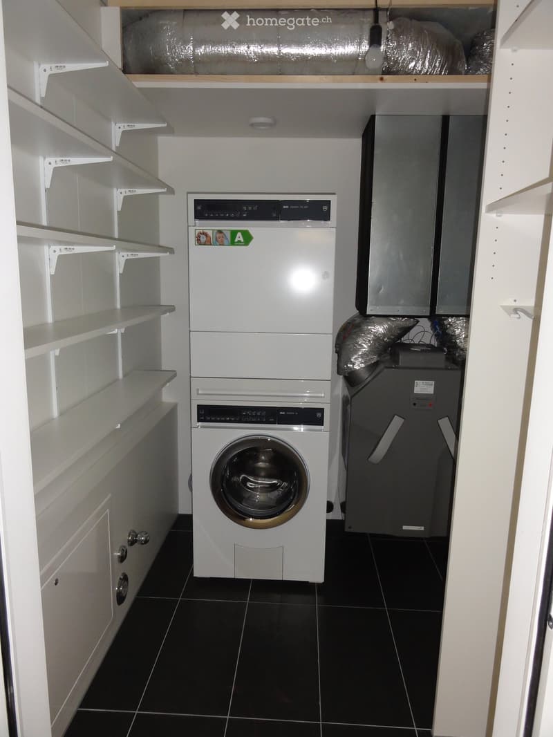 A washer, dryer and air condition unit, all white with grey cabinets, white shelves, and black tiles on the floor.