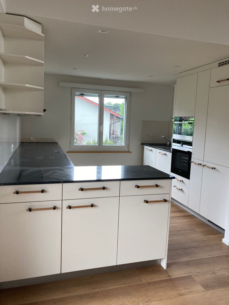 modern kitchen with white cabinets, black countertops, wooden floor, large window, built-in oven and microwave, sink with faucet