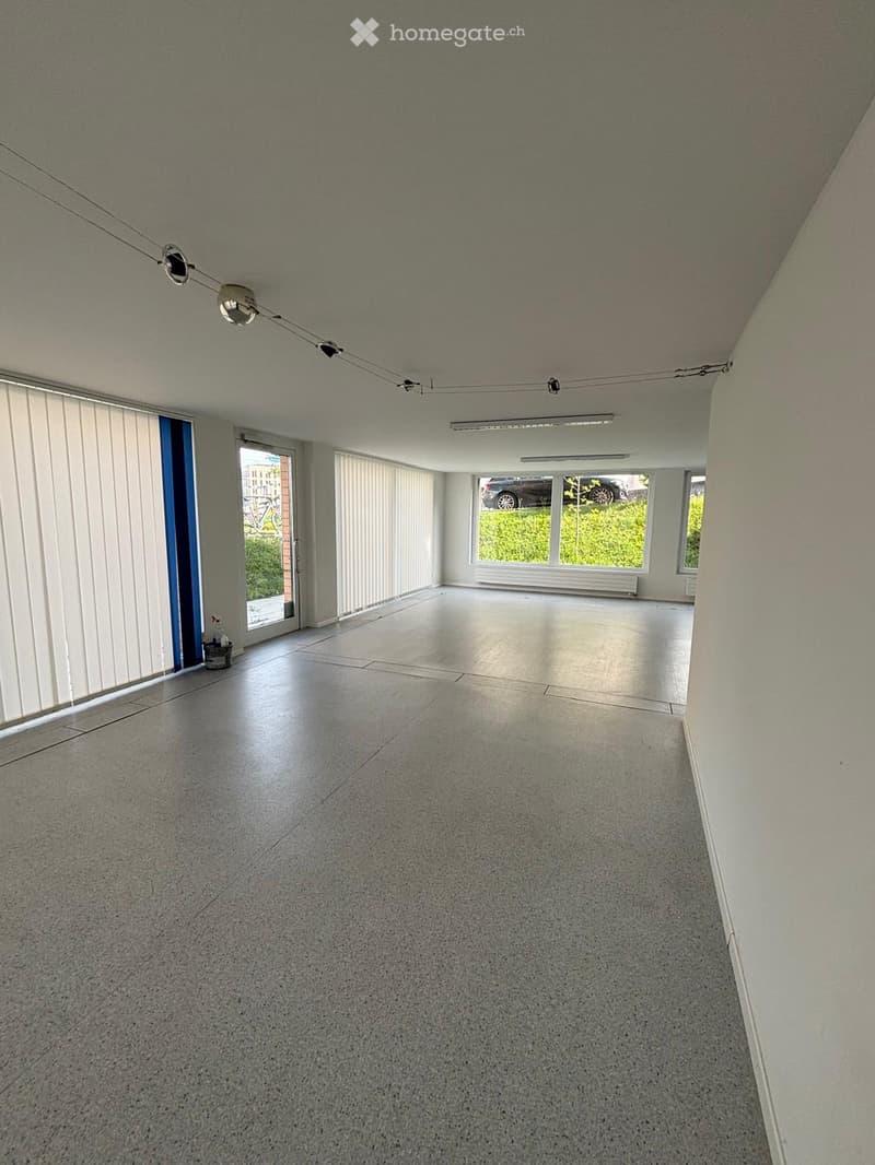 empty room, white walls, gray floor, large windows, white blinds, ceiling lights, door, parking area outside