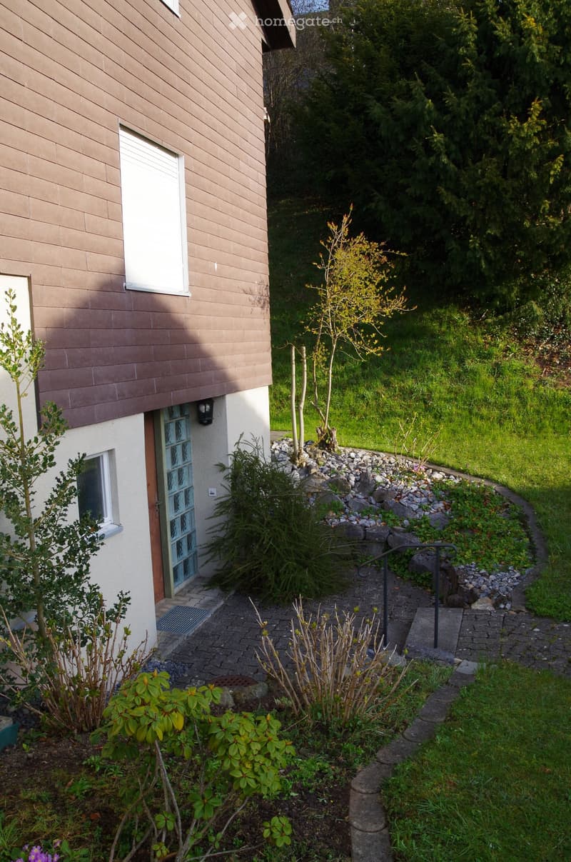 brown brick house, white windows, glass door, gravel path, small garden, trees
