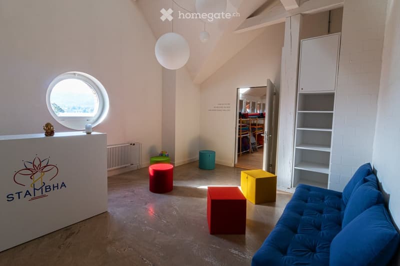 Circular window, white walls, blue sofa, colorful stools, white counter, white shelves, white ceiling lamps