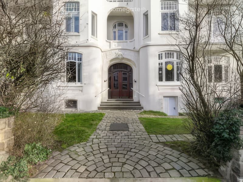 white building, wooden door, stone pathway, multiple windows, arched entrance, small garden