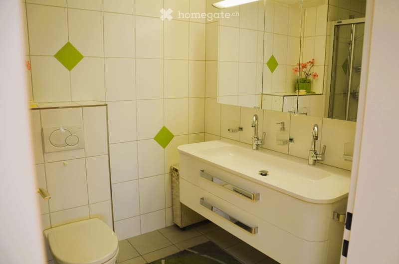 Bathroom with white tiles, white sink, mirror, toilet, and a small rug