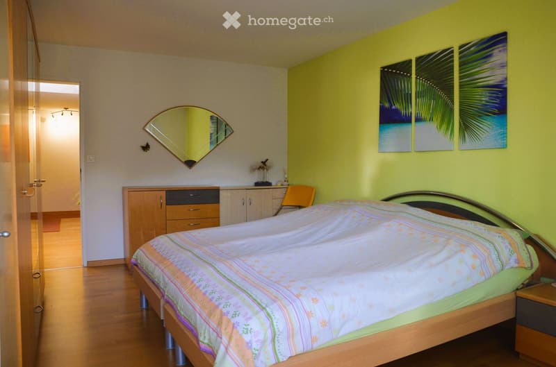 Bedroom with bed, wooden floor, yellow walls, mirror, cabinet, paintings, chair, nightstand