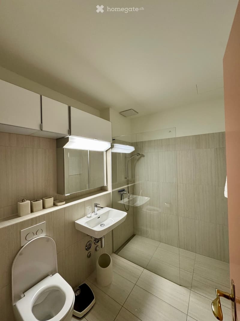 modern bathroom with white tiles, glass shower enclosure, white sink, white toilet, white cabinets, mirror, and a scale