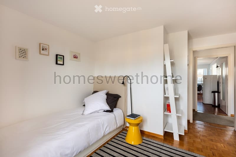 Single bed, white bedding, bedside table, lamp, ladder, rug, picture frames, open door