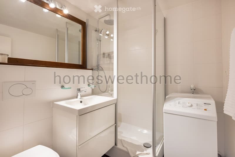 modern bathroom with white tiles, white sink, shower, toilet, washing machine
