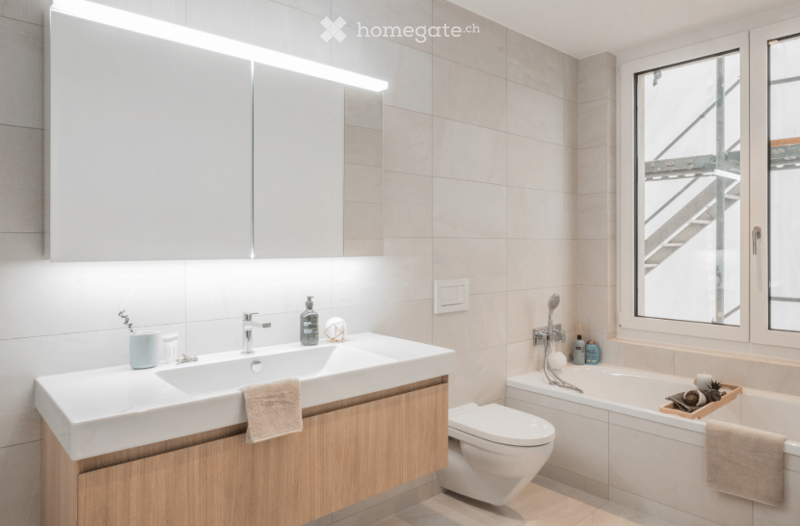 modern bathroom with white tiles, wooden cabinet, white sink, bathtub, toilet, window