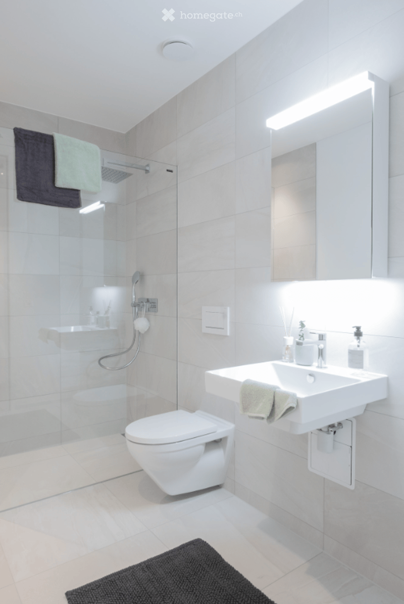 modern bathroom with white tiles, glass shower enclosure, white sink, mirror, towel rack, toilet, and towel
