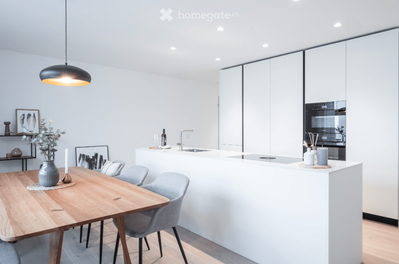 modern kitchen with white cabinets, wooden dining table, gray chairs, pendant light, built-in oven, sink, faucet, countertop, decorative items