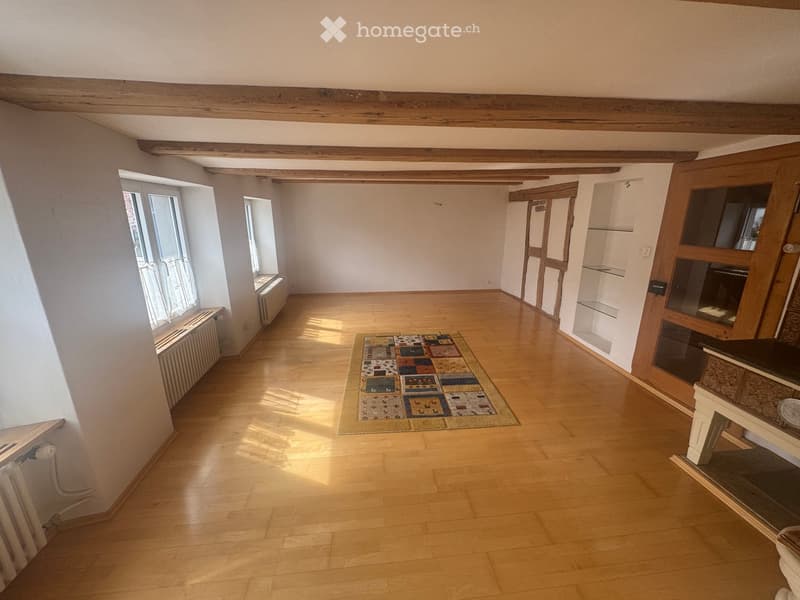 Empty room with wooden floor, wooden beams, windows, radiators, rug, wooden door, glass door, shelves