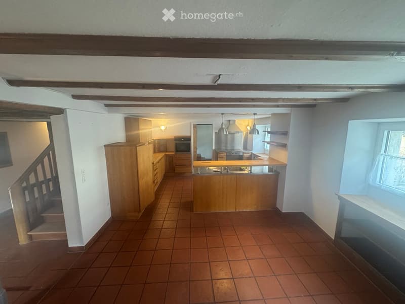 Empty kitchen with wooden cabinets, tiled floor, and a staircase leading to the upper floor.