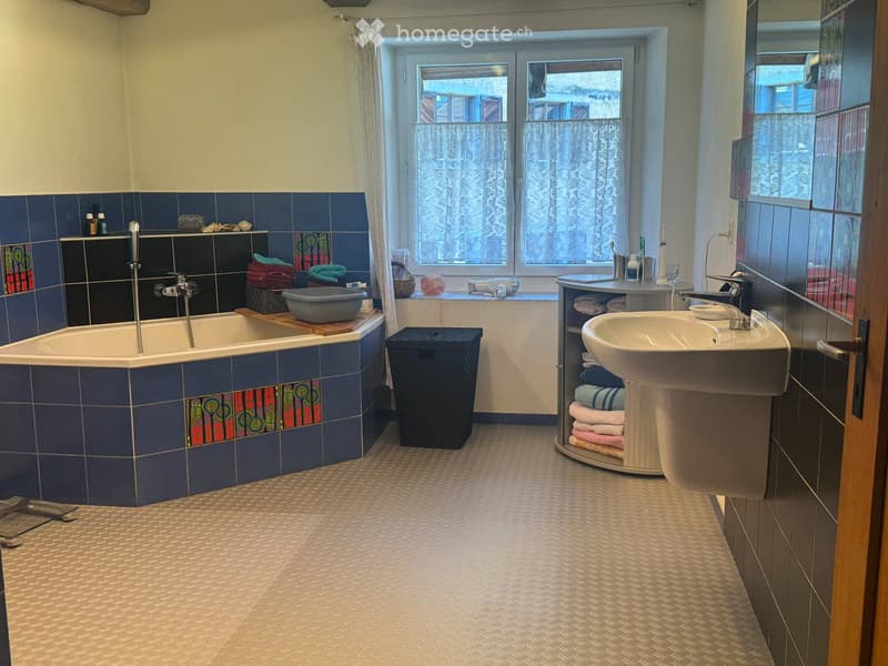 Bathroom with bathtub, sink, and window with curtains, blue tiles, and storage.