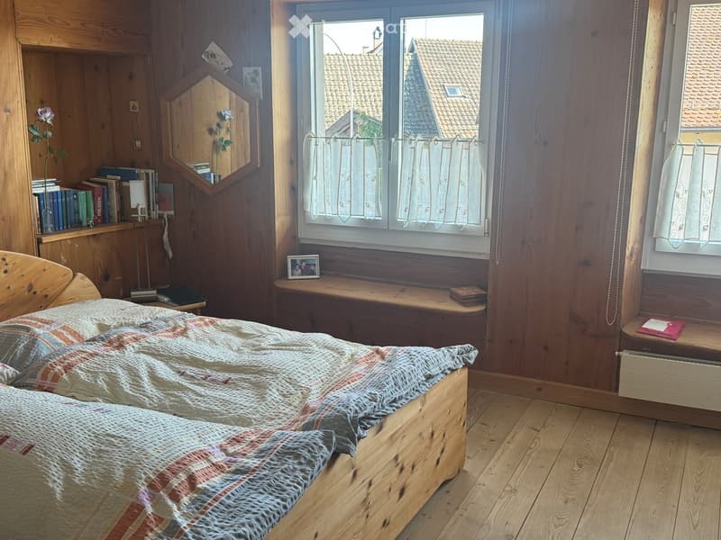 bedroom with wooden bed, wooden shelves, books, picture frame, window with curtains, wooden window seat, radiator