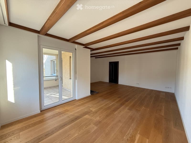 An empty room with wooden floors and white walls, a glass sliding door to a balcony with a view, and a wooden ceiling