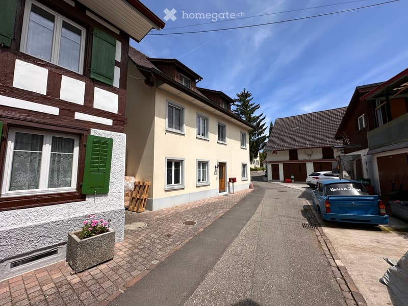 3 story house, brown roof, green shutters, brick sidewalk, blue car parked