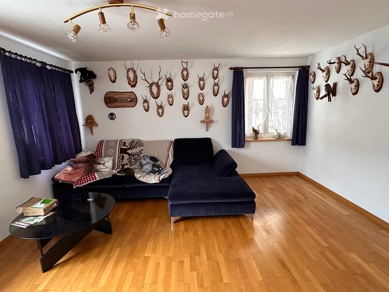 Living room with a couch, coffee table, wooden floor, white walls, and a chandelier