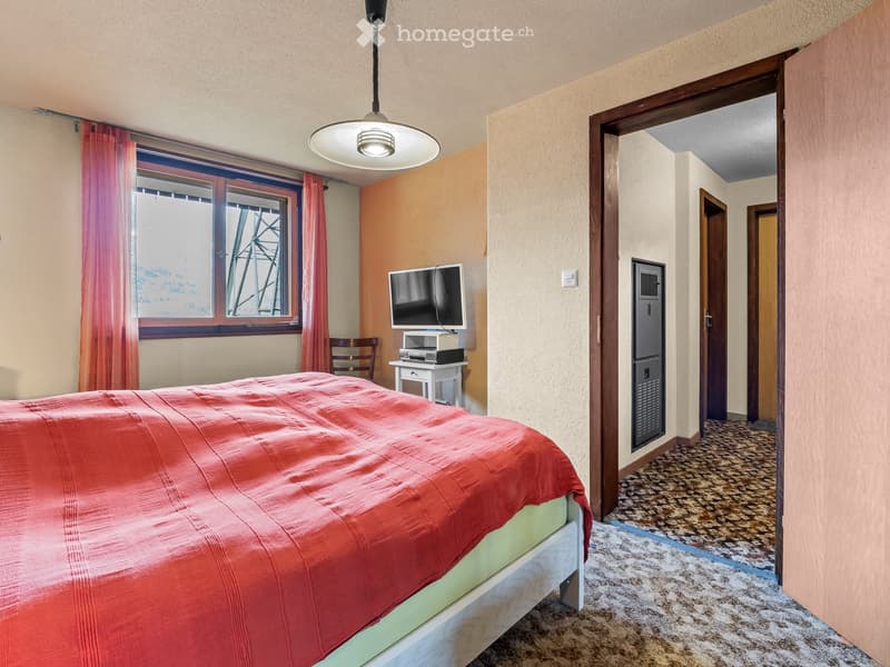 Bedroom with bed, TV, chair, desk, and window with curtains