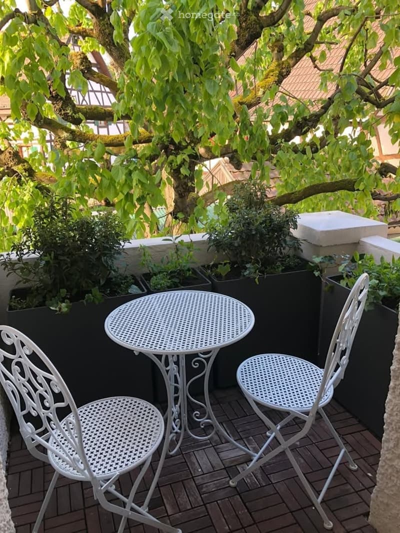 Decorated balcony with tables, chairs, plants, tiled floor, view of trees and buildings
