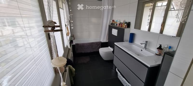 Modern bathroom with white tiles, a bathtub, a toilet, a sink, and a shower curtain