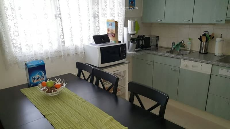 modern kitchen with dining area, green table, black chairs, dining table cloth, fruit bowl, microwave, white cabinet, dishwasher