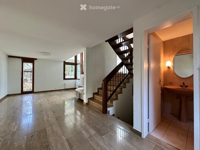 Empty room with wooden floor, white walls, wooden staircase, and a sink with a mirror in the corner.
