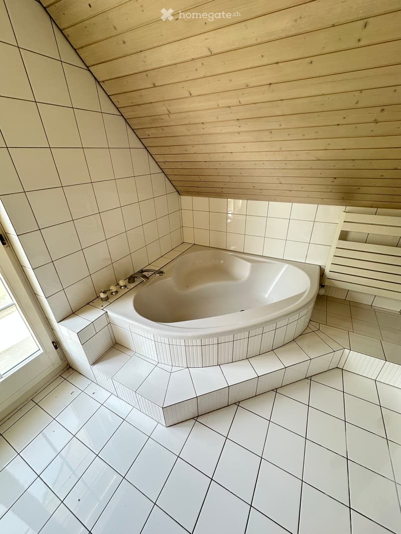 Bathroom with a white bathtub, white tiles, wooden ceiling, and a window