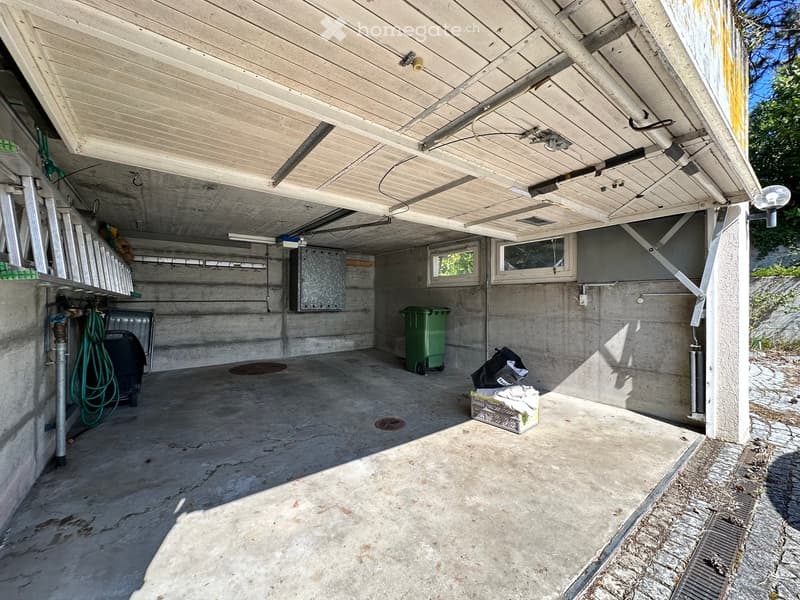 empty garage with concrete floor, metal beams, two windows, two trash bins, and a ladder