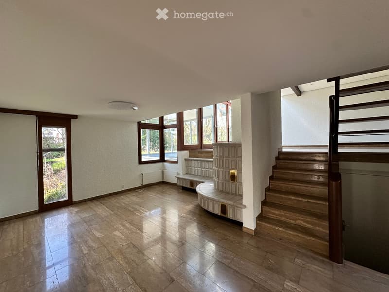 Empty room with wooden floor, white walls, large windows, wooden stairs, and a bench